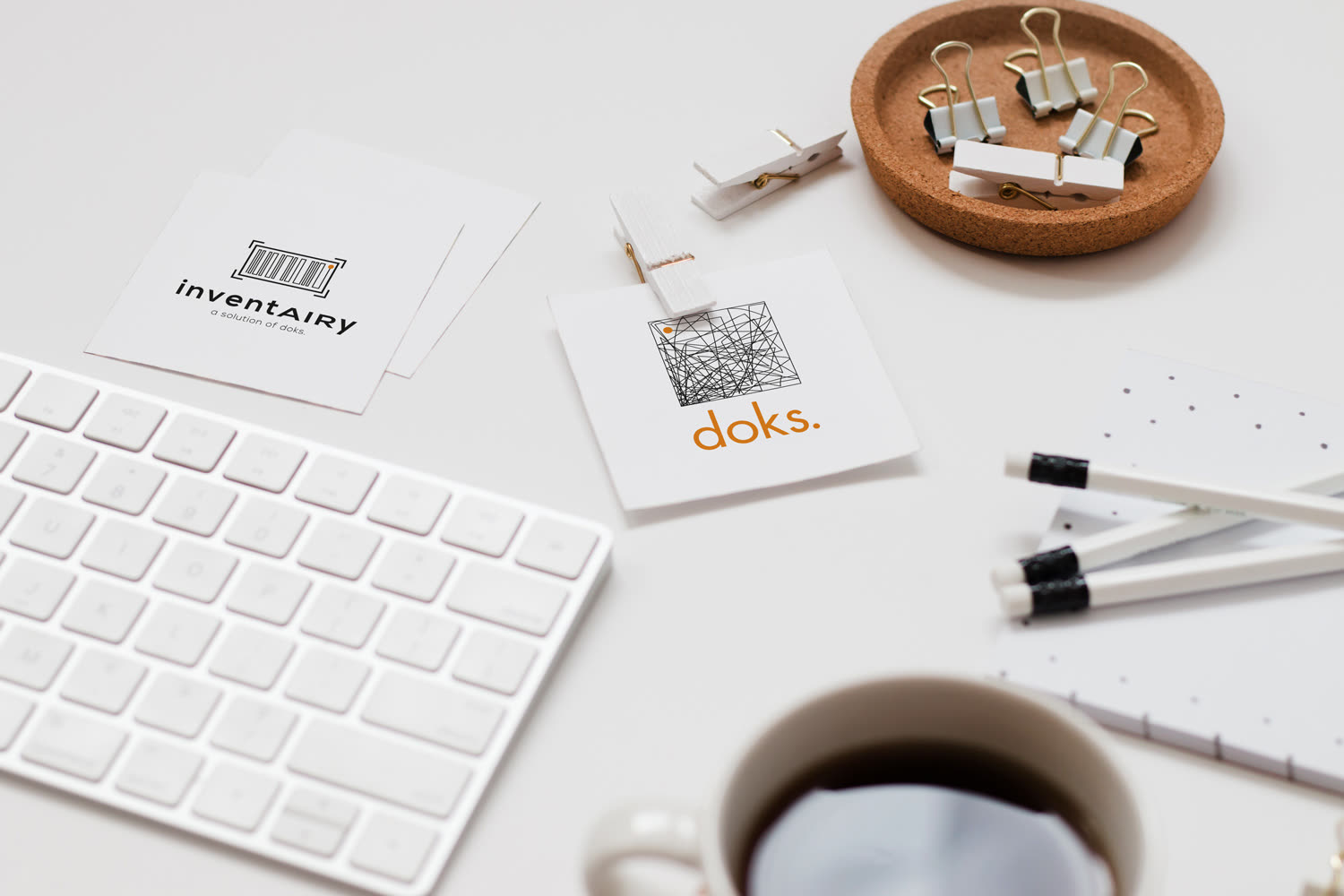 Zwei quadratische Karten auf einem weißen Schreibtisch, darauf die Logos „inventAIRy“ und „doks.“ – ein Geflecht feiner Linien mit einem orangen Punkt.