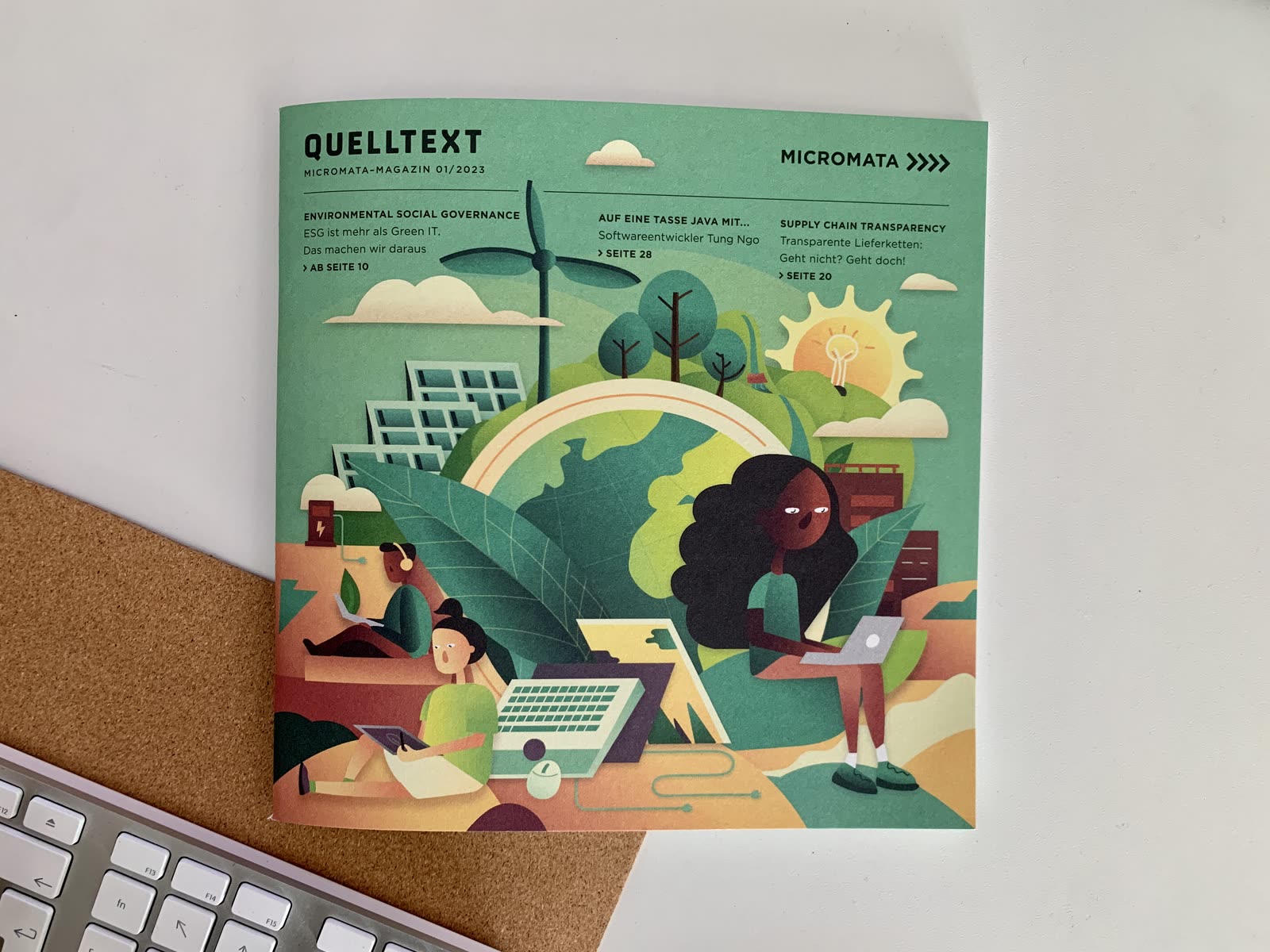 Das gedruckte Magazin Quelltext 01/2023 auf einem Schreibtisch: die Titelillustration zeigt eine grüne Landschaft mit Windrad und Solarfeldern, in der vier Menschen mit Laptops arbeiten.